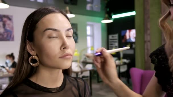 Make-up umělec používá základní tón krém na tvář dívek pomocí štětce v salonu krásy — Stock video