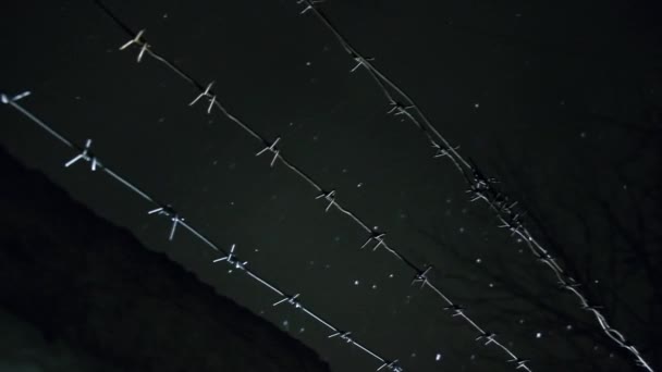 Soğuk, karanlık kış gecesinde, kar yağarken beton çitin üzerinden dikenli teller örülmüş. — Stok video