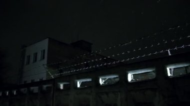 Soğuk, karanlık kış gecesinde, kar yağarken beton çitin üzerinden dikenli teller örülmüş.