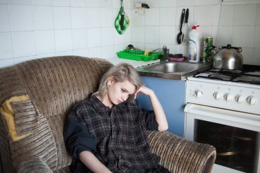 Genç, güzel, kısa saçlı bir bayan eski moda mutfakta koltukta oturuyor.