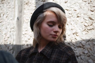 Güneş ışınlarında duvarın yanında oturan kısa saçlı beyaz bir kadın.