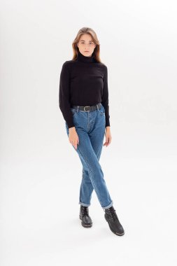 Uzun saçlı, siyah balıkçı yakalı, kot pantolonlu, beyaz bir kadın.