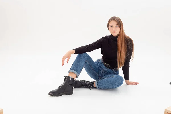 Ung, attraktiv kvinne i svart pologenser, blå jeans i hvitt studio – stockfoto
