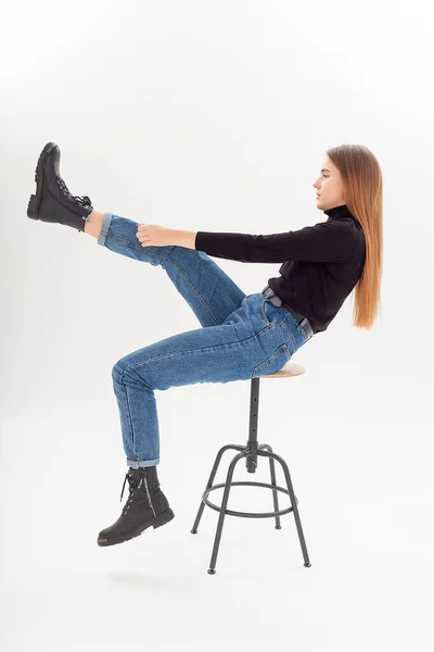 Ung attraktiv kaukasiska kvinna i svart polotröja, blå jeans drar stövlar på — Stockfoto