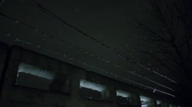 Soğuk, karanlık kış gecesinde, kar yağarken beton çitin üzerinden dikenli teller örülmüş.