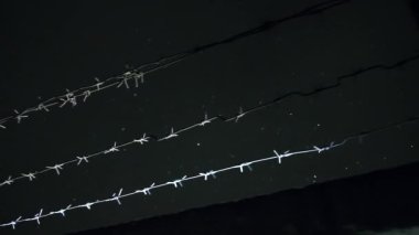 Soğuk, karanlık kış gecesinde, kar yağarken beton çitin üzerinden dikenli teller örülmüş.