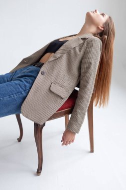 Stüdyoda çenesi yukarıda, sandalyeye uzanmış uzun saçlı beyaz bir kadın.