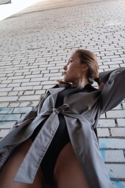 Trençkotlu çekici Asyalı model, alt noktadan duvarın yanında duruyor.