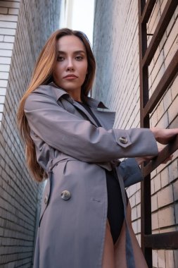 Asyalı çekici manken duvardaki yangın merdiveninde duran trençkot giyiyor.