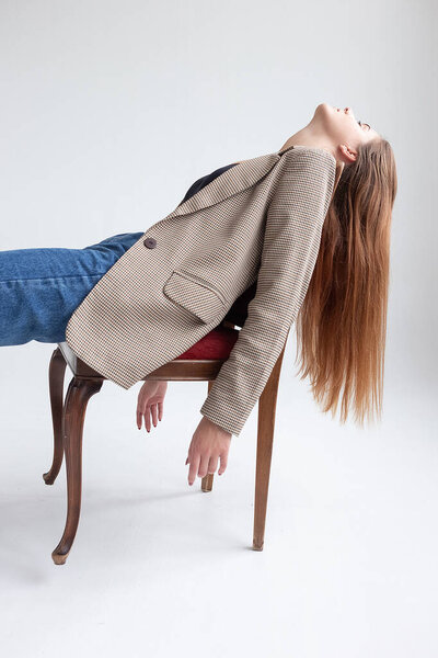 молодая белая женщина с длинными волосами, лежащая на стуле в студии с поднятым подбородком