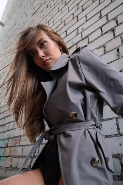 Atraente asiático modelo no trincheira casaco de pé perto parede tiro a partir de menor ponto — Fotografia de Stock
