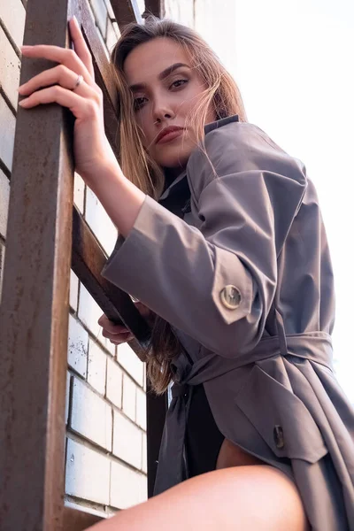 Aziatische aantrekkelijke model dragen trench jas staan op brandladder op muur — Stockfoto