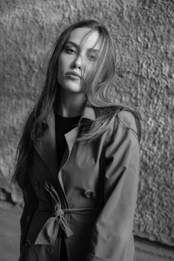 Gri trençkotlu çekici Asyalı model dışarıda duvarın yanında duruyor.