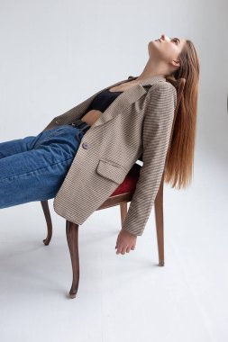 Stüdyoda çenesi yukarıda, sandalyeye uzanmış uzun saçlı beyaz bir kadın.