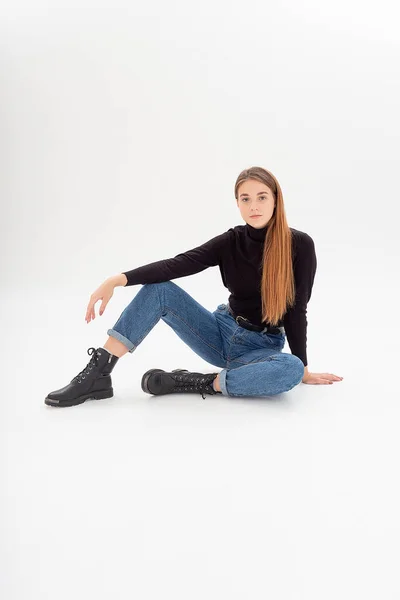 Young attractive caucasian woman in black turtleneck, blue jeans at white studio — Stock Photo, Image