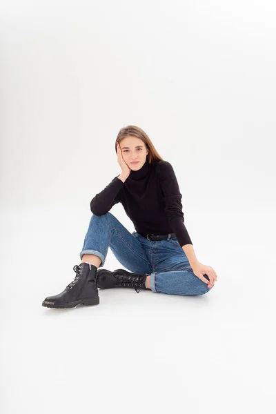 Giovane attraente donna caucasica in dolcevita nero, jeans blu in studio bianco — Foto Stock