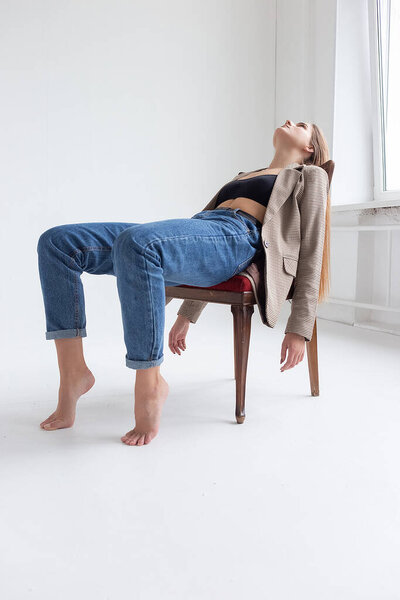 молодая белая женщина с длинными волосами, лежащая на стуле в студии с поднятым подбородком