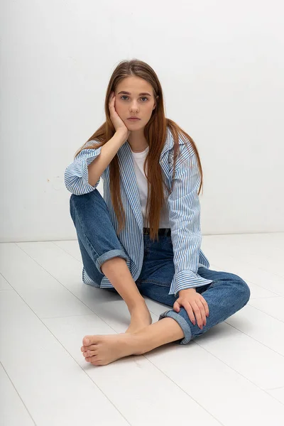 Jovem caucasiano bonita menina com cabelos longos na camisa, jeans azul senta-se no estúdio — Fotografia de Stock