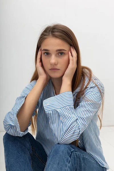 Junges kaukasisches hübsches Mädchen mit langen Haaren im blau gestreiften Hemd sitzt im Studio — Stockfoto