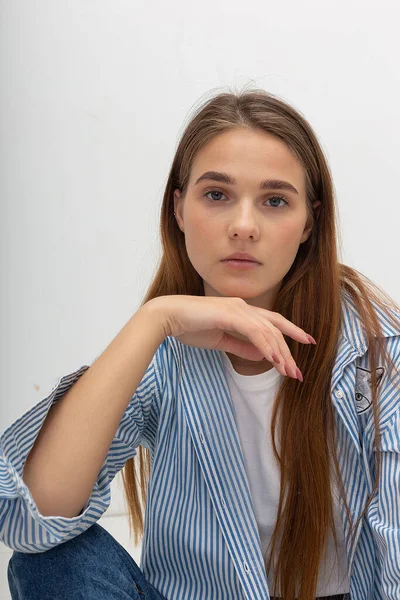 Young caucasian pretty girl with long hair in blue striped shirt sits at studio — Stock Photo, Image