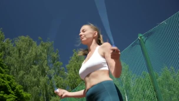 Jeune femme en vêtements de sport ne saute exercice au terrain de sport avec corde à sauter — Video