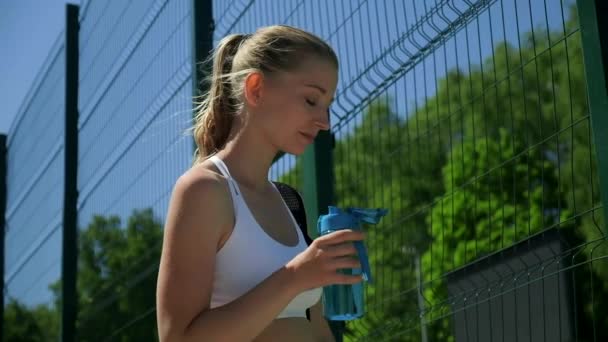 Ung kaukasisk kvinna släcker sin törst. hona dricker vatten från blå flaska — Stockvideo