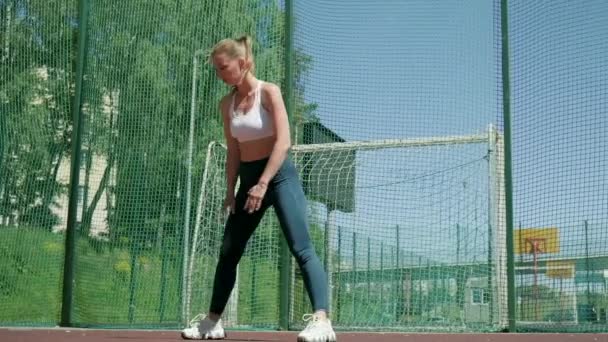 Ung sportig blond flicka i sportkläder gör övningar utomhus på idrottsplats — Stockvideo