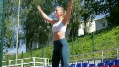 Beyaz tenli güzel kadın spor sahasında hoplayıp zıplıyor ve el çırpıyor.