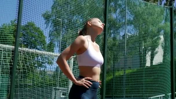 Młody dopasowany blondynka cycata kobieta w odzież sportowa rozciągając jej szyję na boisko sportowe — Wideo stockowe