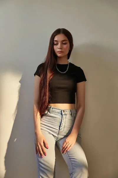 Portrait of young caucasian girl with long hair in jeans standing next to wall — Stock Photo, Image