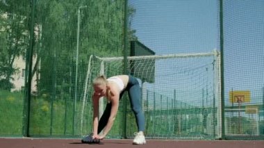 Spor kıyafetli genç sarışın kız spor sahasında egzersiz yapıyor.