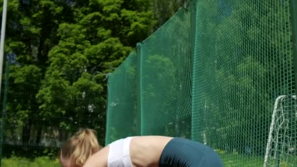 Jeune fille blonde sportive en vêtements de sport fait des exercices à l'extérieur au terrain de sport — Video