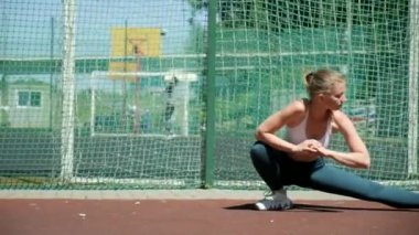 Spor giysileri içinde spor sahasında bacaklarını esneten genç, formda güzel bir kadın.