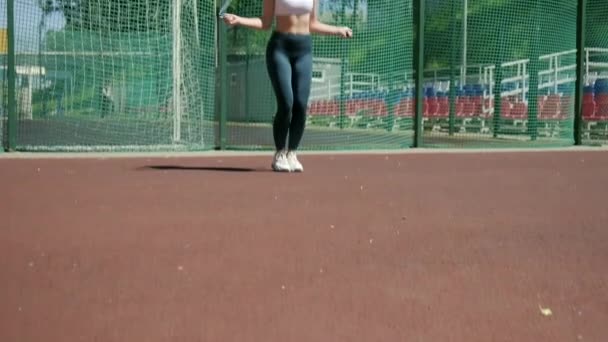 Ung kvinna i sportkläder gör hoppa motion på idrottsplats med hopprep — Stockvideo