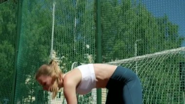 Spor kıyafetli genç sarışın kız spor sahasında egzersiz yapıyor.