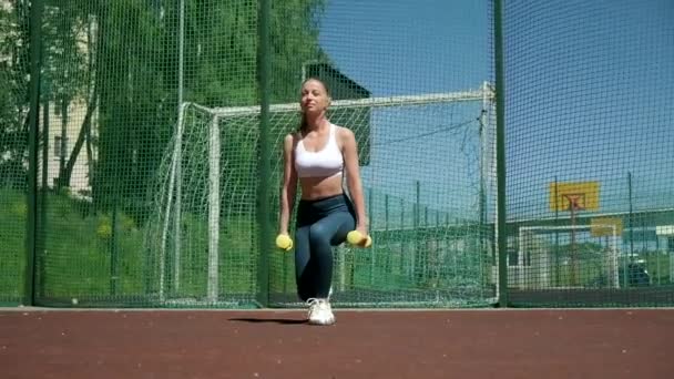 Genç formda sporcu kız spor sahasında dambıllarla hareket ediyor. — Stok video