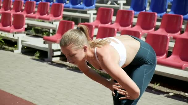 Young fit busty woman with ponytail in sportswear stretching at sports ground — Stockvideo
