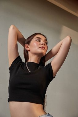 Boynunda zincir olan, uzun saçlı, duvarın yanında duran beyaz bir kız.