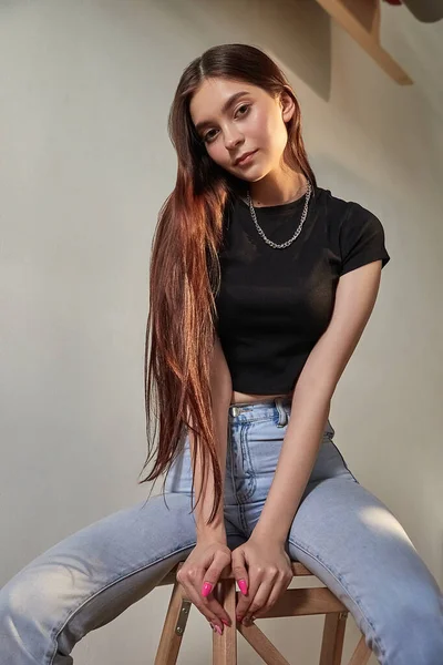 Retrato de chica caucásica joven con el pelo largo en jeans sentados en taburete de madera — Foto de Stock