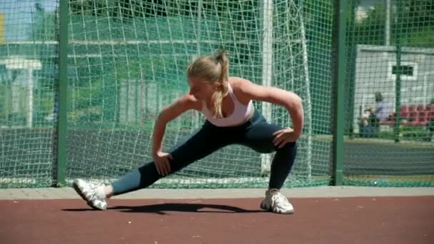 Joven en forma deportiva bonita hembra en ropa deportiva piernas estiradas en el campo de deportes — Vídeo de stock