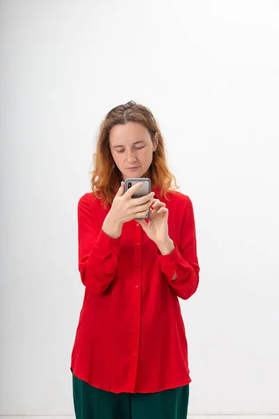 Young concentrated caucasian redheaded woman uses mobile phone, searching on web — Stok fotoğraf