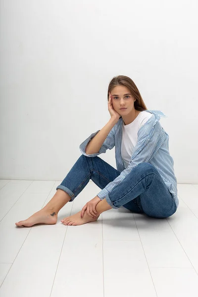 Jeune caucasien jolie fille avec les cheveux longs en chemise, jeans bleu se trouve au studio — Photo