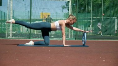 Formda atletik bir kadın spor sahasında pilates ringi ile tahtada duruyor.