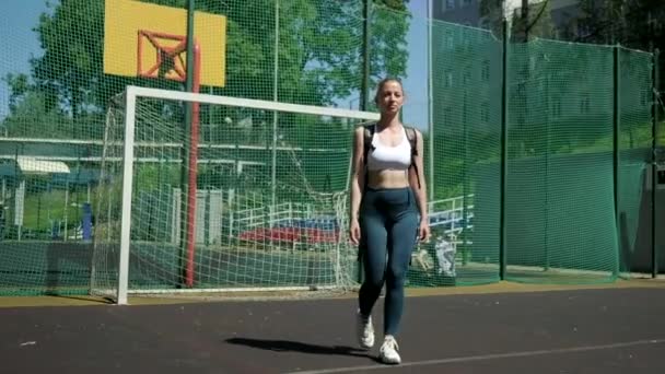Молода спортивна блондинка з хвостом у спортивному одязі, що йде на спортивному майданчику — стокове відео