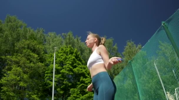 A fiatal nő a sportszerkóban ugrál a sportpályán ugrókötéllel. — Stock videók