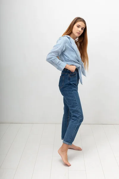 Young caucasian pretty girl with long hair in shirt, blue jeans poses at studio — Stock Photo, Image