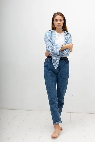 Young caucasian pretty girl with long hair in shirt, blue jeans poses at studio — Stockfoto