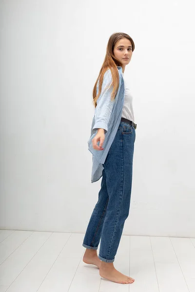 Young caucasian pretty girl with long hair in shirt, blue jeans poses at studio — Stock Photo, Image