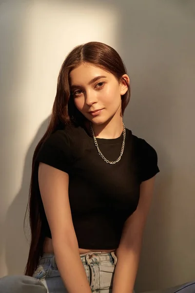 Potret gadis kaukasia muda dengan rambut panjang dengan celana jeans duduk di sebelah dinding — Stok Foto