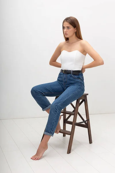 Young caucasian woman with long brown hair in in corset, blue jeans at studio — Stock Photo, Image